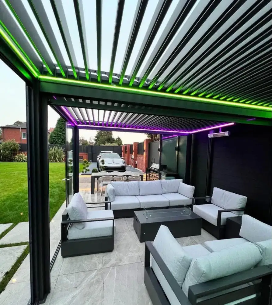 Dark slatted pergola above pale outdoor sofas with green and purple feature lighting and a lawn alongside