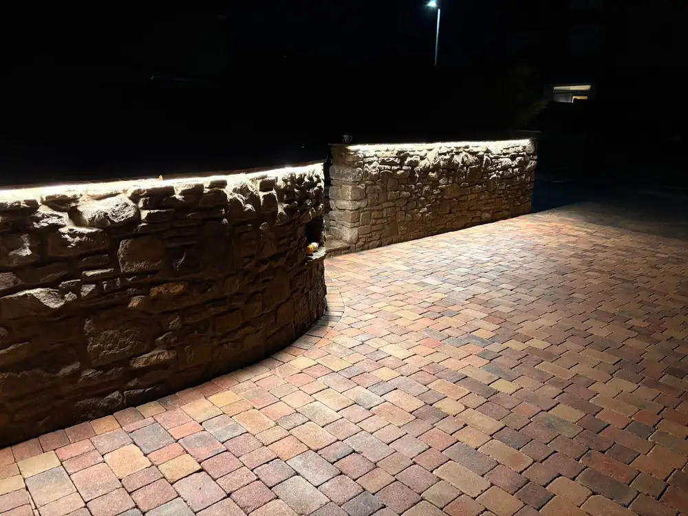Mixed-tone block paving beside a curved stone wall illuminated along its top edge at night