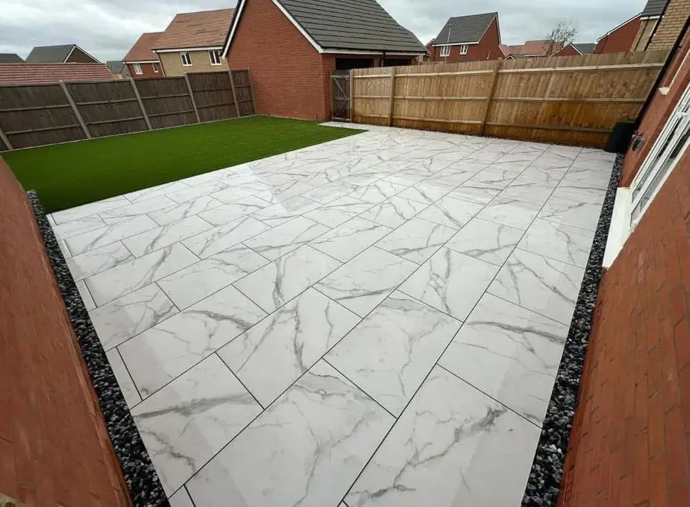 White marble-effect patio with grey veining beside a rectangular green lawn area and timber fencing